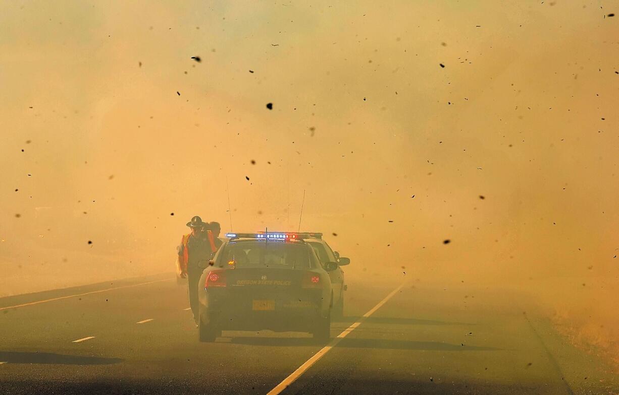 An Oregon State Police trooper dodges ash from a fire burning along Interstate 5 near Rogue River, Ore., on Thursday.