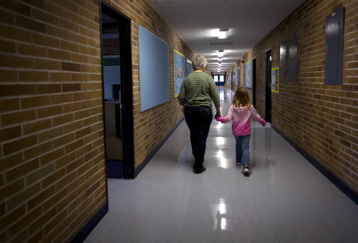 Staff assistant Sharleen Smith escorts a student to her first-grade class at Ellsworth Elementary School, as school began Wednesday in the Evergreen, Hockinson, La Center and Ridgefield school districts.