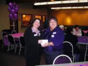 Michelle Bart, president of Soroptimist International of Southwest Washington, presents a contribution to Debra Adams, director of YWCA SafeChoice, during the Purple Lights Bingo event.