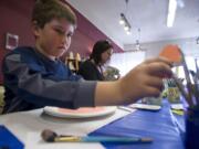 Jasyn Howland, 9, reaches for a paint brush while he decorates a plate for his ninth birthday at Earth Glaze and Fire pottery on Main Street.