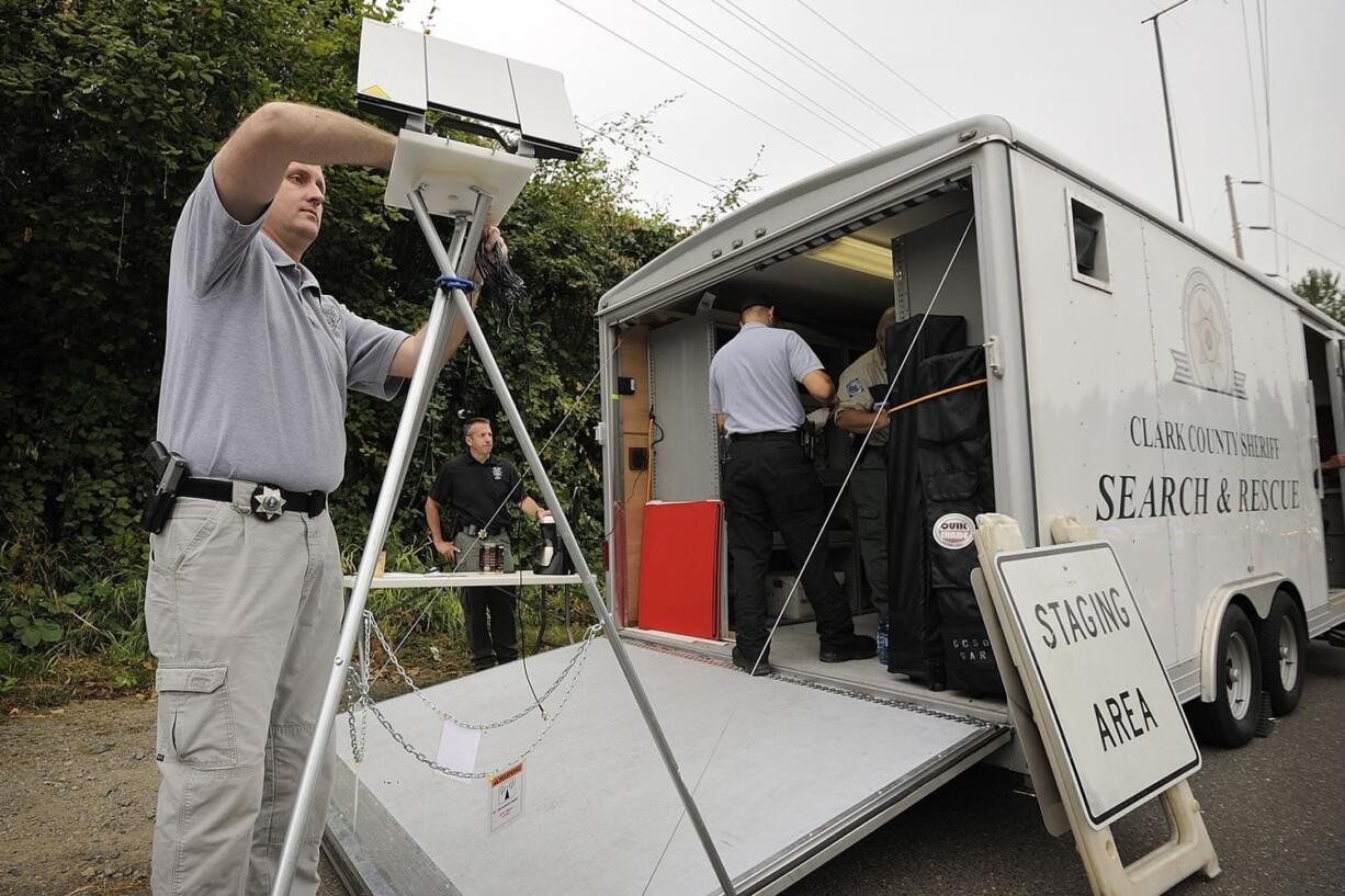 Clark County Deputy Jim Payne, left, sets up a satellite transceiver at the Salmon Creek Greenway trail head Saturday. More than two dozen individuals, K-9 units and six search and rescue teams searched for Craig Spydell, whose car was found parked at the trail head on Sept. 12.