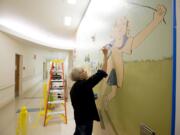 Retired art teacher Rebecca Anstine paints a mural Thursday at the entrance of the pediatric emergency department at Legacy Salmon Creek Medical Center.