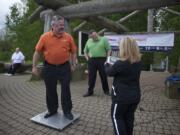 Washougal Mayor Sean Guard, in orange shirt, steps on the scale as Camas Mayor Scott Higgins, in green shirt, watches during the launch of the community weight-loss challenge, &quot;Camas and Washougal On A Diet,&quot; on Wednesday at Capt. William Clark Park in Washougal.