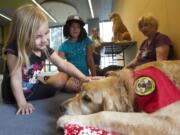 Lola Fuller, 6, left, and Sofia Arellano, 9, meets Columbia River Pet Partners therapy dog Crunch, a golden retriever. The children practiced their reading skills by reading to him at the Vancouver Community Library on Aug. 13, 2014. Therapy animal handler Michael Kay Richardson watches at rear.