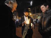 Flame of freedom: Yakov Kartashev, left, holds a torch as Rabbi Shmulik Greenberg, center, lights a flame and Vancouver Mayor Tim Leavitt waits to light the first candle at the annual menorah lighting in Esther Short Park on Tuesday. Greenberg reminded the crowd that Hannukah, the eight-day Jewish festival of light, is really a festival of freedom.