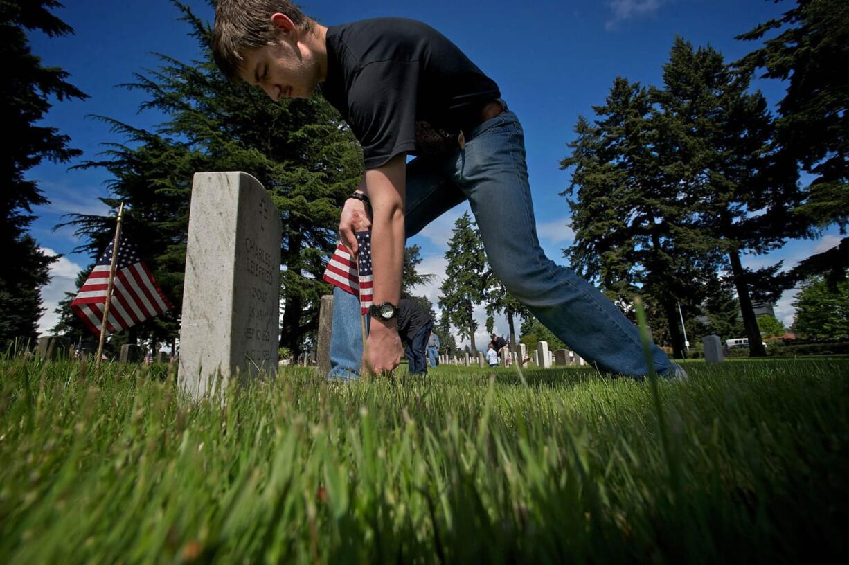 Forrest White, 17, places a flag at a grave marker Thursday at the Post Cemetery in preparation for the Memorial Day weekend.