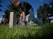 Forrest White, 17, places a flag at a grave marker Thursday at the Post Cemetery in preparation for the Memorial Day weekend.