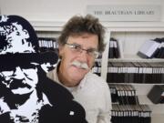 John F. Barber, with the Creative Media &amp; Digital Culture Program at Washington State University Vancouver, holds a cardboard cutout next to a display of The Brautigan Library at The Clark County Historical Museum.