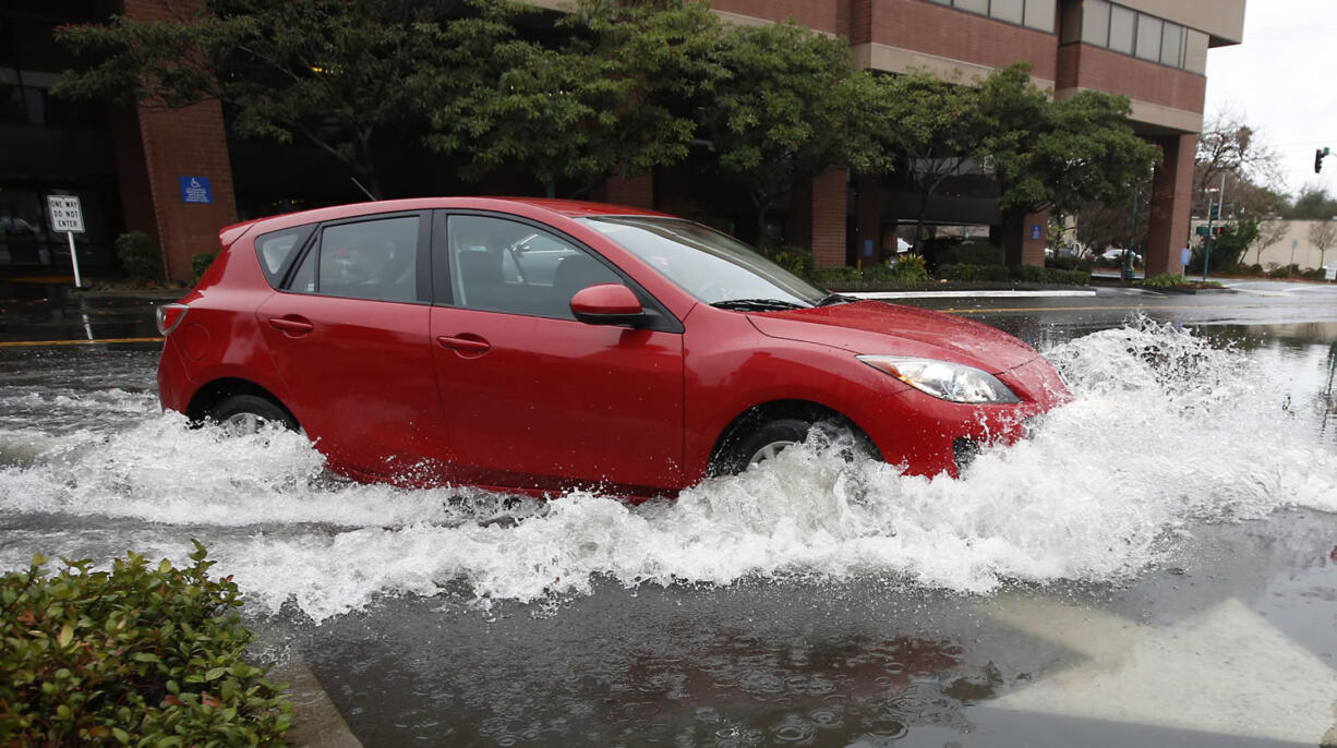 A car navigates through a flood water as it turns into a parking lot Tuesday in Sacramento, Calif. El Nino storms lined up in the Pacific promise to drench parts of the West for more than two weeks and increase fears of mudslides and flash floods in regions stripped bare by wildfires.