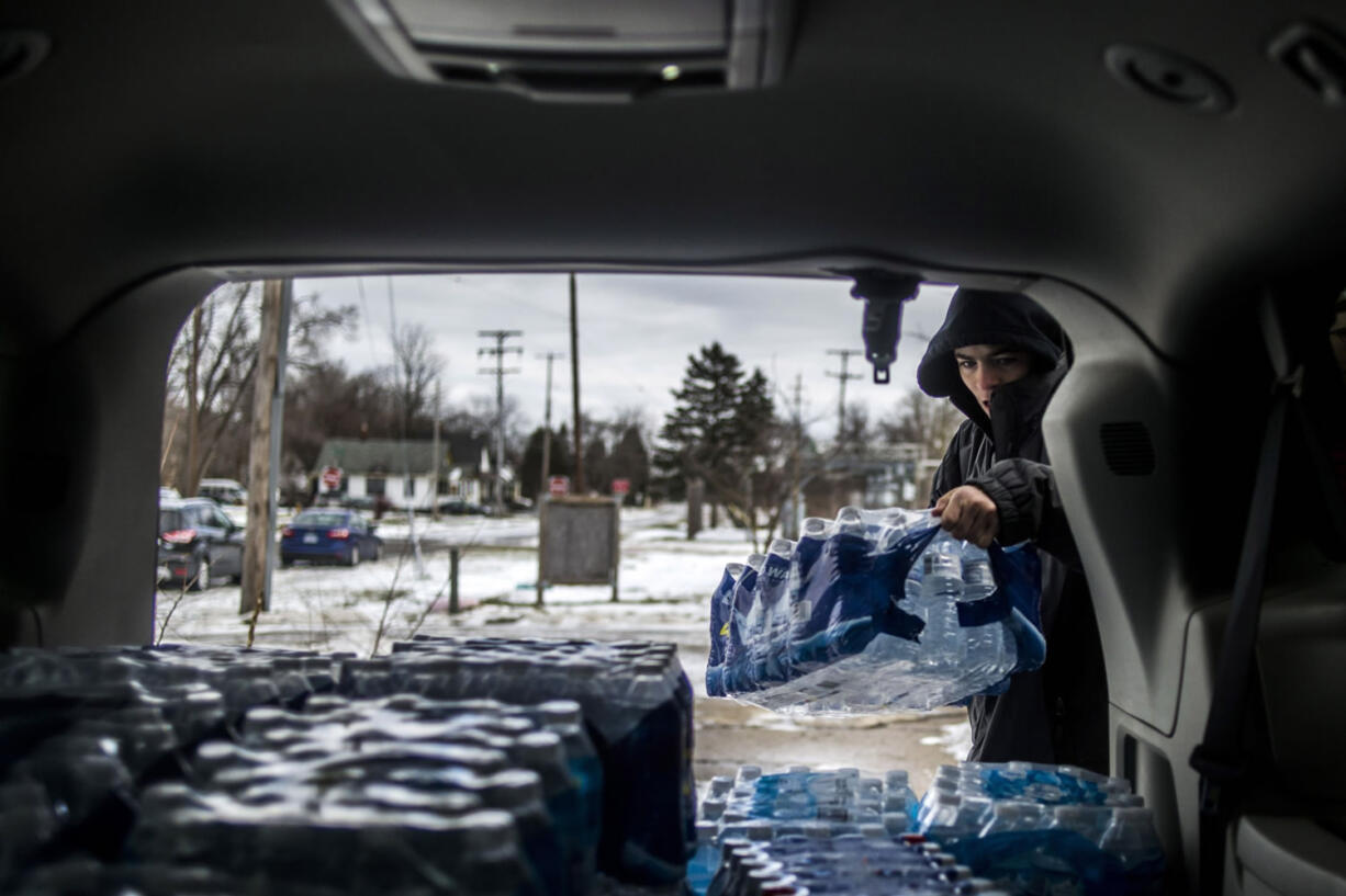 Flint, Mich., resident Randy Huyck Jr., 17, throws a case of bottled water into the back of a volunteer&#039;s car Saturday as Detroit-area volunteers drop off more than 500 cases of bottled water in Flint.