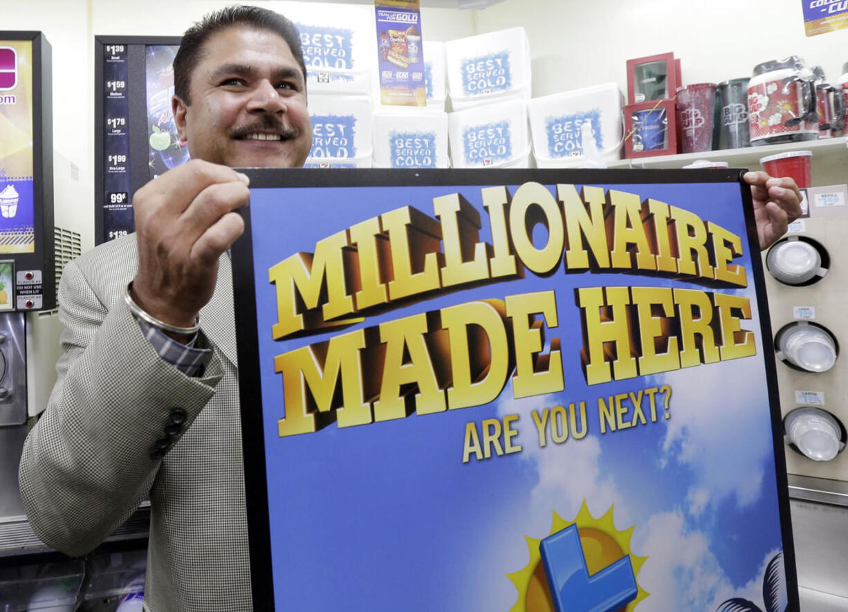 Balbir Atwal, the owner of a 7-Eleven store that sold a winning Powerball lottery ticket, holds up a Millionaire Made Here sign Thursday at his store in Chino Hills, Calif.
