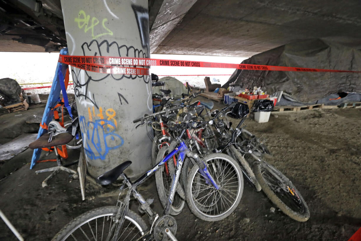 Bicycles remain stacked Wednesday against a support post for Interstate 5 as crime scene tape surrounds the site of a shooting the night before at a homeless encampment in Seattle.