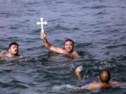 Lefteris Chrisomallos from Greece holds up a wooden cross after he retrieved it during an Epiphany ceremony Wednesday in Izmir, Turkey.