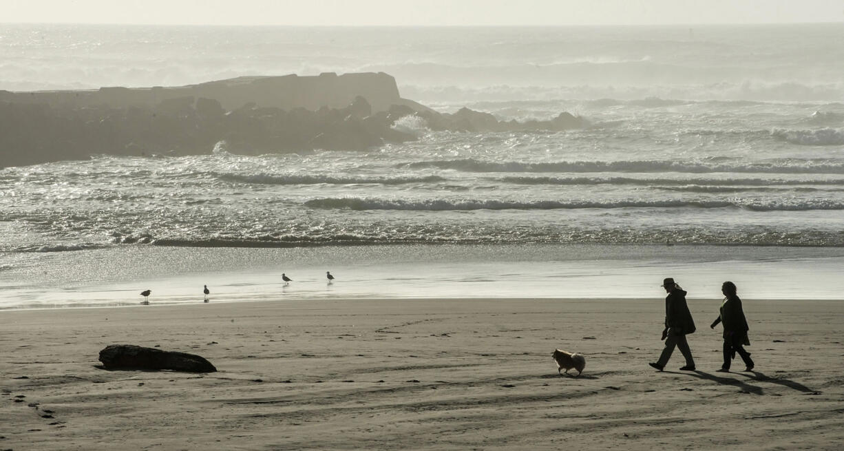 A couple walks their dog along the beach at Bullards Beach State Park in Bandon, Ore., near the Coquille River jetty.