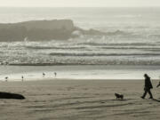 A couple walks their dog along the beach at Bullards Beach State Park in Bandon, Ore., near the Coquille River jetty.