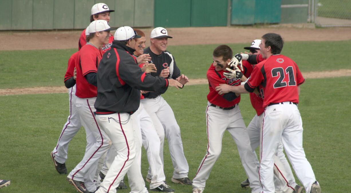 Camas baseball players and coaches celebrate with Justin Webb (center) after he beat out the base hit that won the district title Thursday, at Propstra Park in Vancouver.