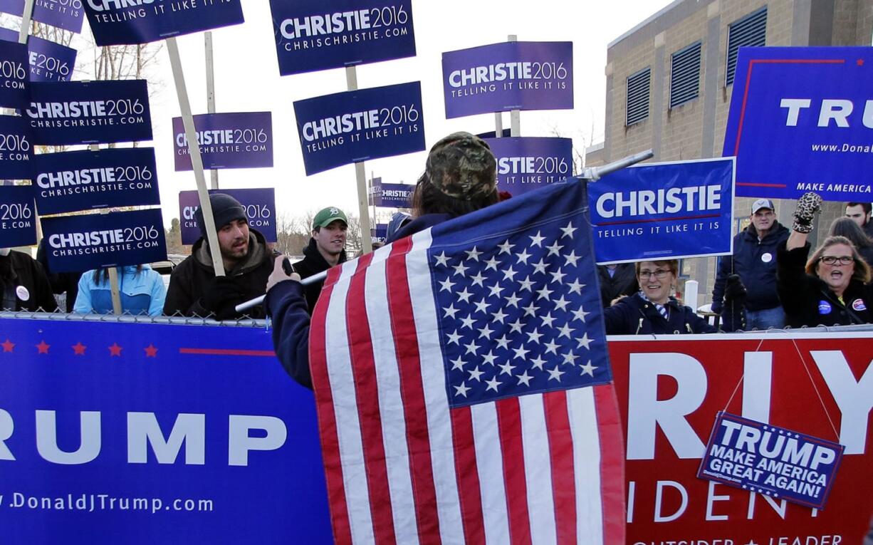 Rod Webber of Boston holds an American flag as he talks with presidential candidate volunteers holding signs outside a polling station on primary day in Londonderry, N.H., on Tuesday.