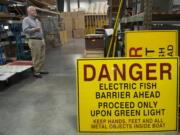 Smith-Root CEO Jeff Smith stands near electric fish barrier warning signs in the company's shop in Salmon Creek.