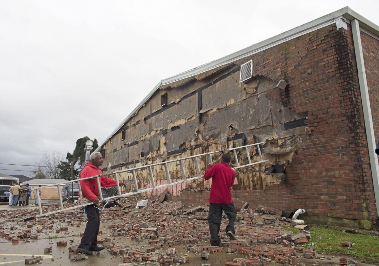 Volunteers Percy Mitchell, 62, left, and Eugene Trice, 38, carry a ladder as they attempt to knock down bricks from the wall of the New Mount Bethel Baptist Church, which suffered weather damage Tuesday in Kenner, La. A massive storm system caused damage throughout the region.