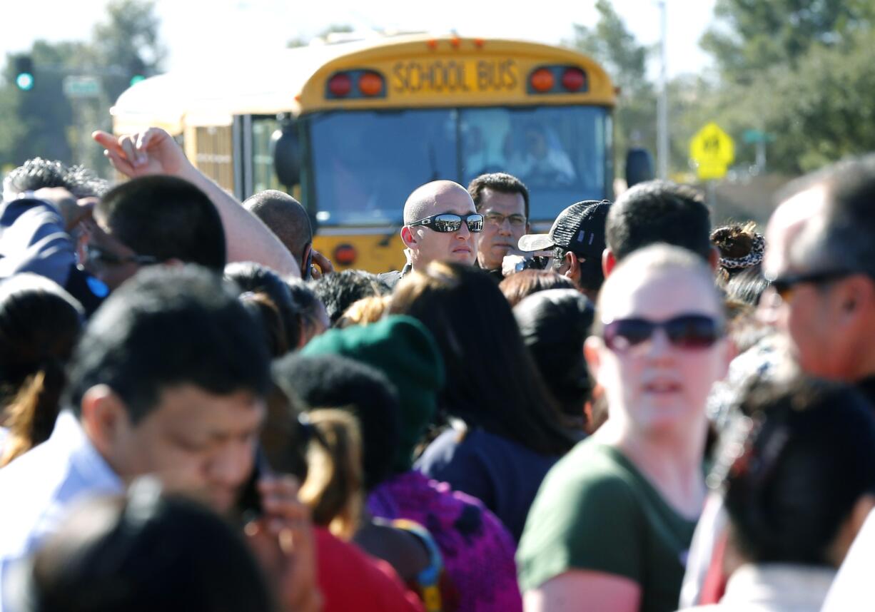 A Phoenix police officer, center, tries to give instructions to parents waiting to board buses to reunite with their children, Friday, Feb. 12, 2016, in Glendale, Ariz., after two students died in a shooting at Independence High School in the Phoenix suburb.