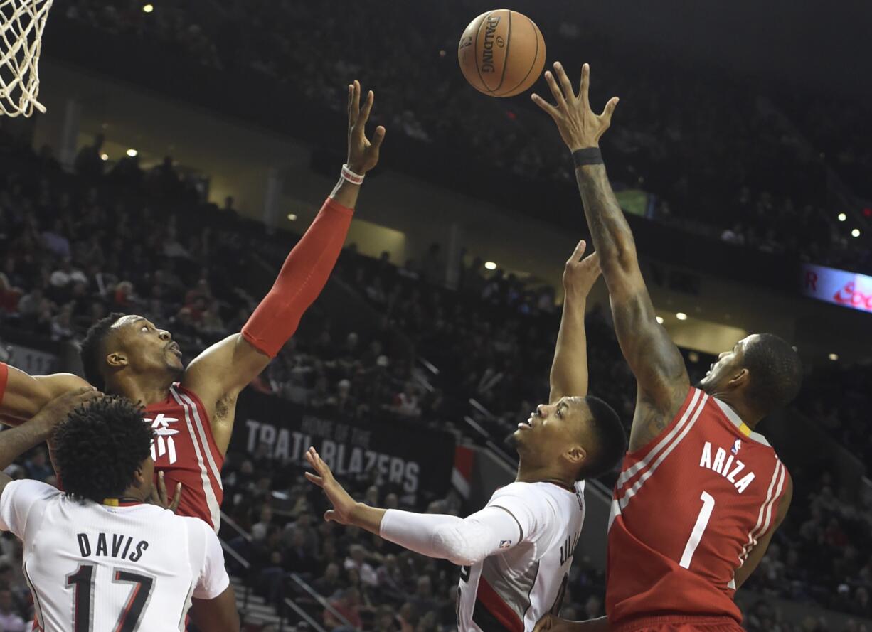 Portland Trail Blazers guard Damian Lillard (0) drives to the basket on Houston Rockets center Dwight Howard (12) and forward Trevor Ariza (1 ) during the second half of an NBA basketball game in Portland, Ore., Wednesday, Feb. 10, 2016. The Blazers won the game 116-103.