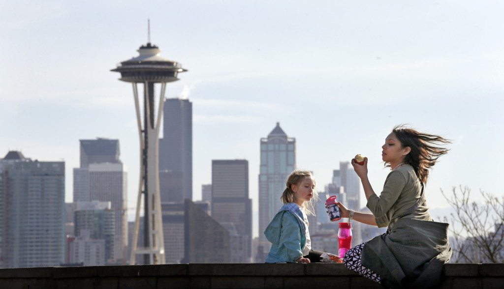 Nora Kennelly, 3, picnics with her nanny, Ty Messiah, in the sun atop a wall overlooking the Space Needle and downtown Seattle on Monday.