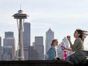 Nora Kennelly, 3, picnics with her nanny, Ty Messiah, in the sun atop a wall overlooking the Space Needle and downtown Seattle on Monday.