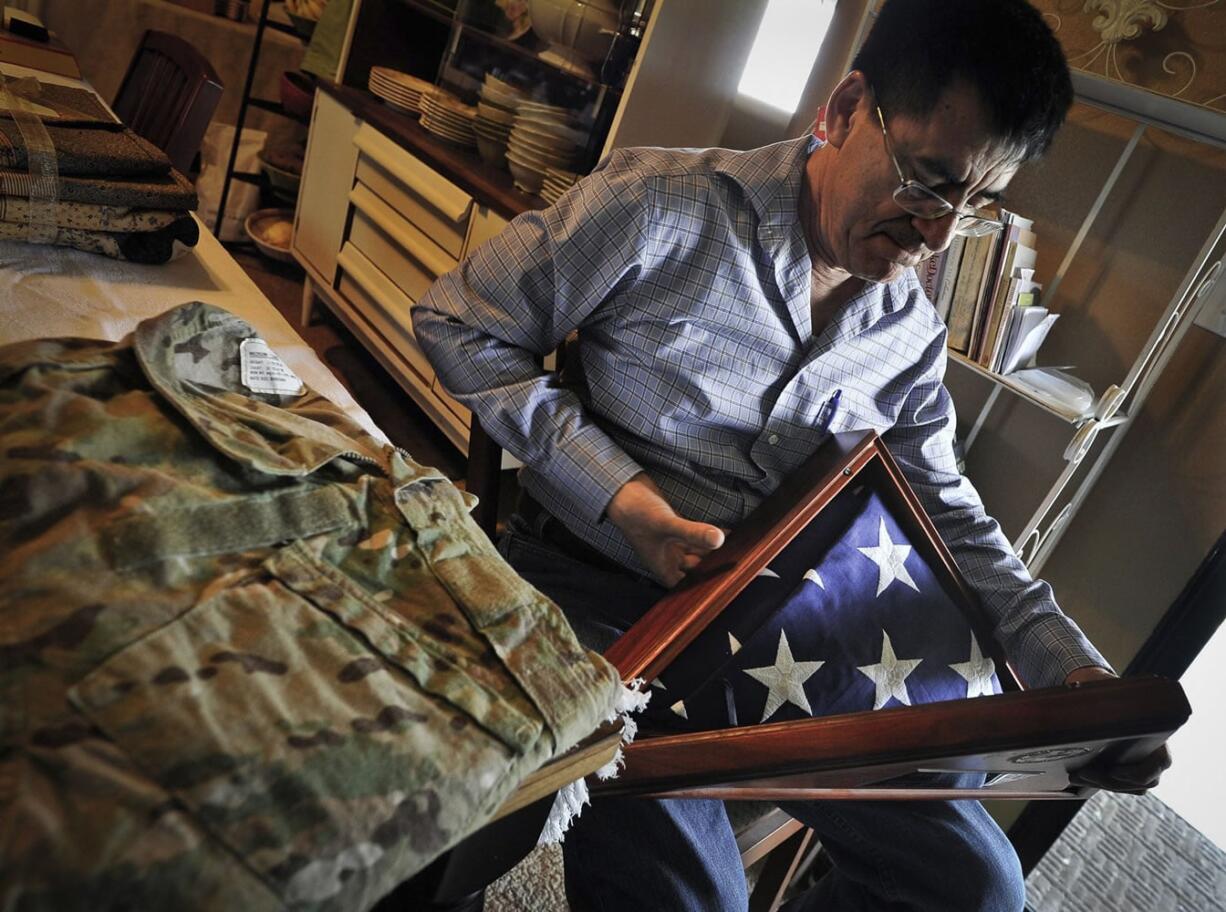 Next to the camouflage uniform of his late son, Army National Guard Spc. Benjamin Pleitez, Salvador Pleitez looks at the flag that draped his casket after he was killed in Mazar-e-Sharif, Afghanistan in 2012.