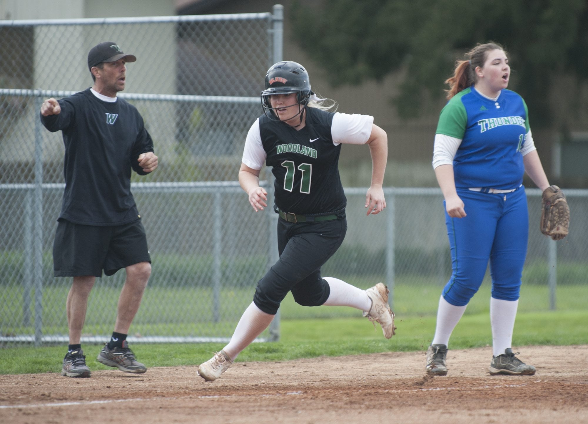 Softball player Jessica Flanagan of Woodland (C) runs past third base, as Mountain View's Tiffany Becker shouts for backup, at a game in Vancouver Monday March 28, 2016.