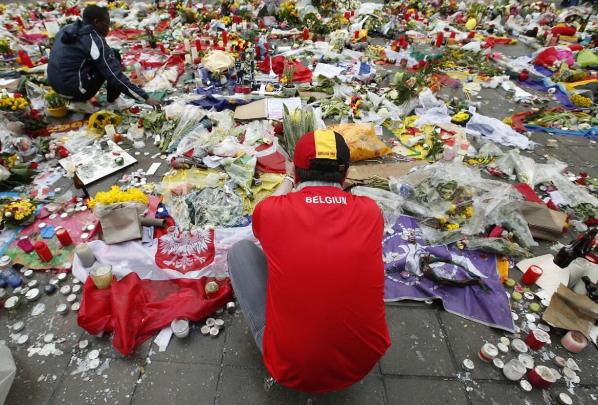 Two men help re-adjust the tributes left for the victims of the recent bomb attacks in Brussels, following heavy rain in the Place de la Bourse in Brussels on Monday.