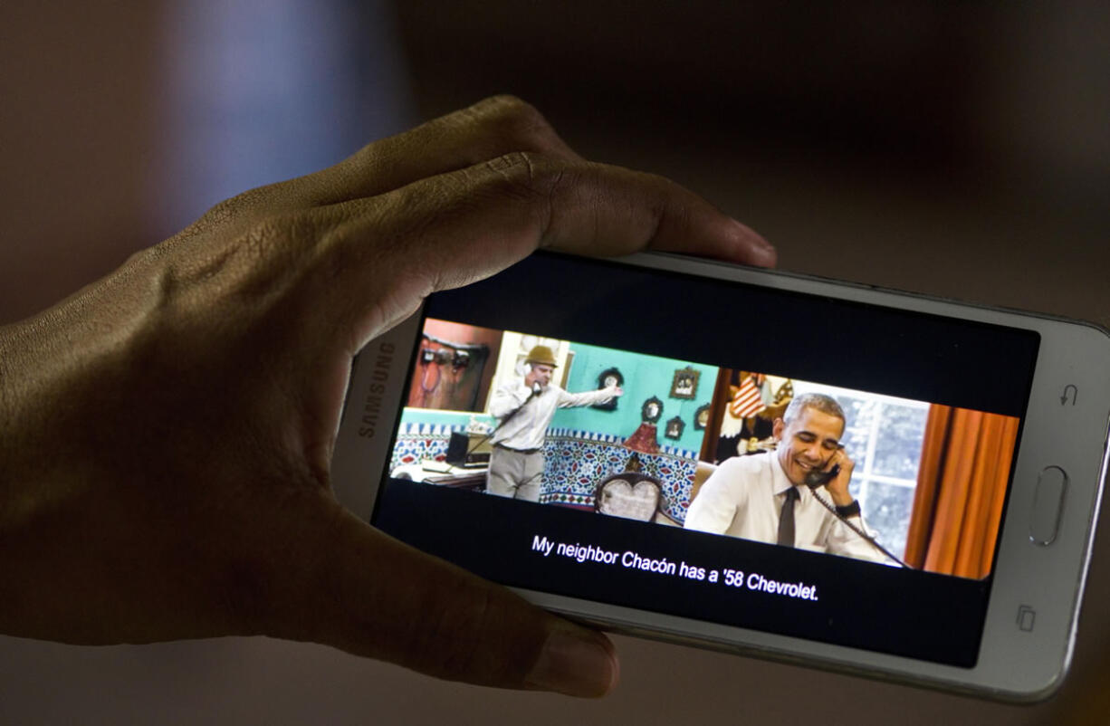 A woman in Havana, Cuba, poses for a photo, holding her cellphone that shows a frame from the video released by the White House of President Barack Obama joking with Cuban comedian Panfilo. The video released Saturday shows Panfilo calling the White House to find out the weather for a baseball game during Obama's trip to Cuba. Obama answers and banters with Panfilo, using Cuban slang to say Panfilo! Get outta here!