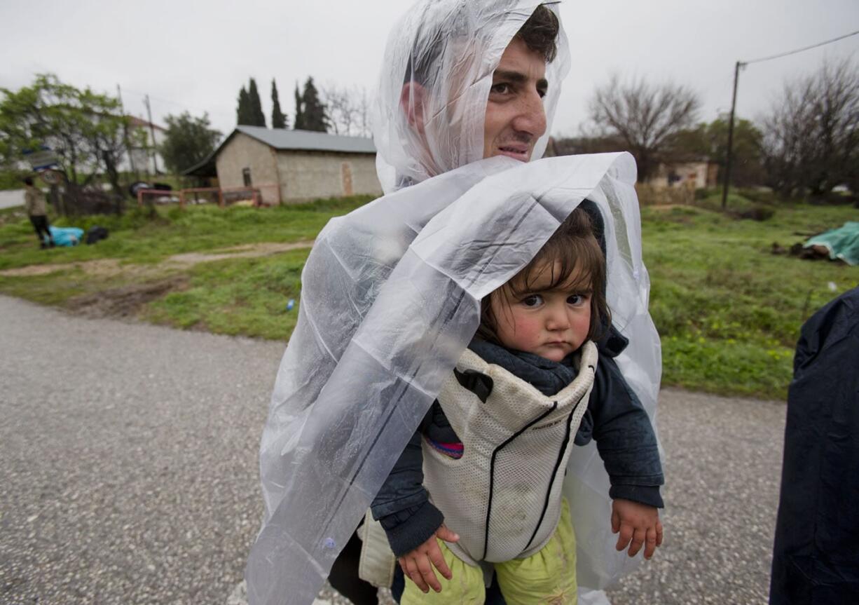 A migrant carries a baby along a road Tuesday north of Idomeni, Greece, after they were turned back from Macedonia. Hundreds of people walked out of an overcrowded migrant camp Monday on the Greek-Macedonian border, determined to use a dangerous crossing to head north, but they were returned to Greece.