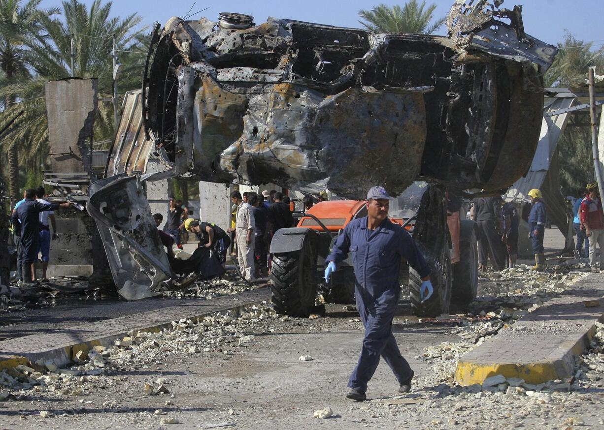 Civilians and security forces gather Sunday as municipality workers remove destroyed vehicles at the scene of a deadly suicide bomb attack in Hillah, about 60 miles south of Baghdad, Iraq.