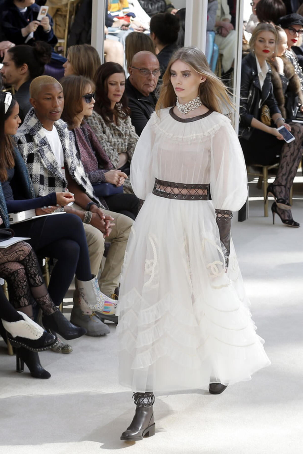 A model walks in front of, from left, Helen Lasichanh, Pharrell Williams, Isabelle Huppert and Anna Mouglalis, wearing a creation for Chanel&#039;s Fall-winter 2016-17 ready-to-wear collection presented Tuesday in Paris.