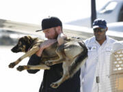 Conner Lamb carries Luna, a 1 1/2-year-old dog that fell off a fishing boat in February, after Luna arrived by a Navy commuter flight Wednesday at Naval Base Coronado in California. Luna was found Tuesday on San Clemente Island, a Navy-owned training base 70 miles off San Diego.