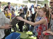 Brett &quot;Mr. Lizard&quot; Wilson, left, introduces a black and white Tegu lizard to Sara Flindt and Jana Flindt, right, during the Earth Day Fest at Salmon Creek Regional Park in Vancouver on Saturday.