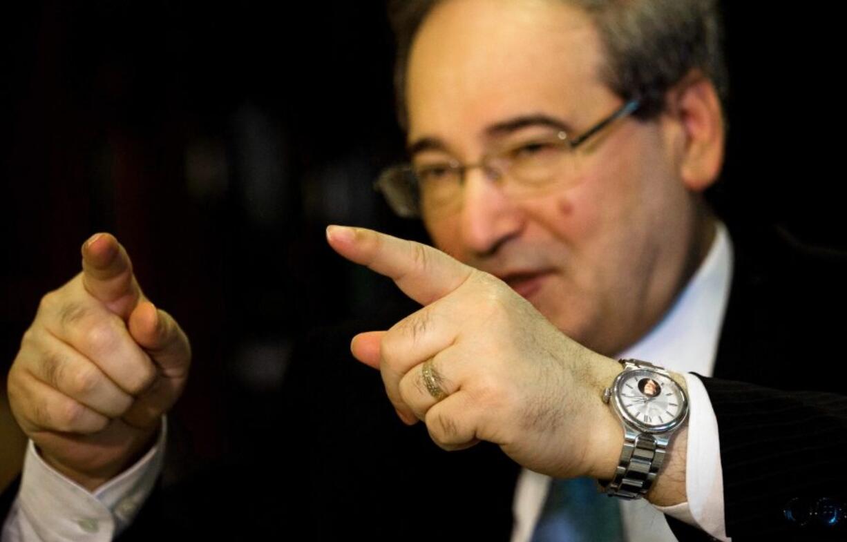 A picture of Syrian President Bashar Assad is seen on the watch of Syrian Deputy Foreign Minister Faisal Mekdad as he speaks Wednesday during an interview with The Associated Press at his office in Damascus, Syria.