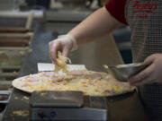 Tayler Smith of Papa Murphy&#039;s sprinkles cheese on a take-and-bake pizza at the East Mill Plain Boulevard store.