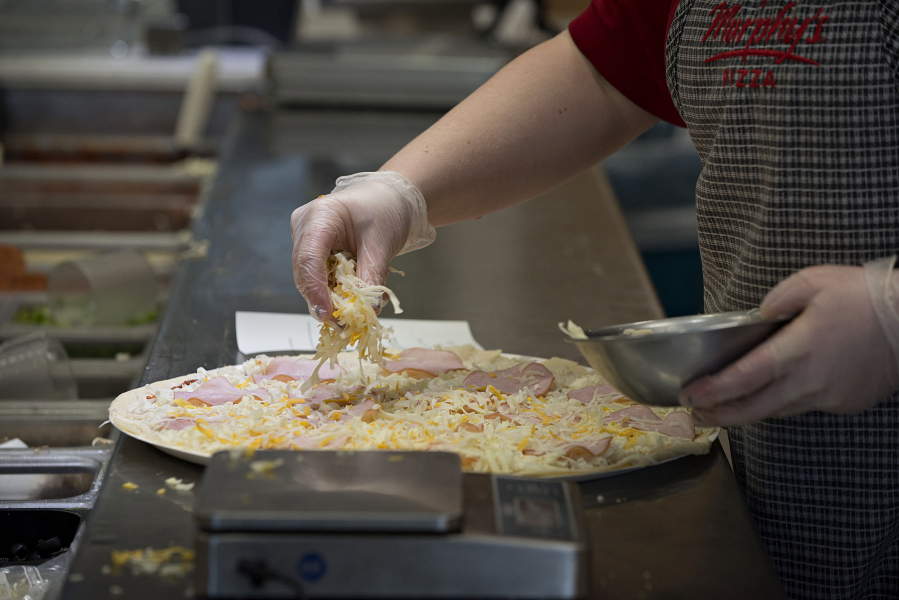 Tayler Smith of Papa Murphy&#039;s sprinkles cheese on a take-and-bake pizza at the East Mill Plain Boulevard store.