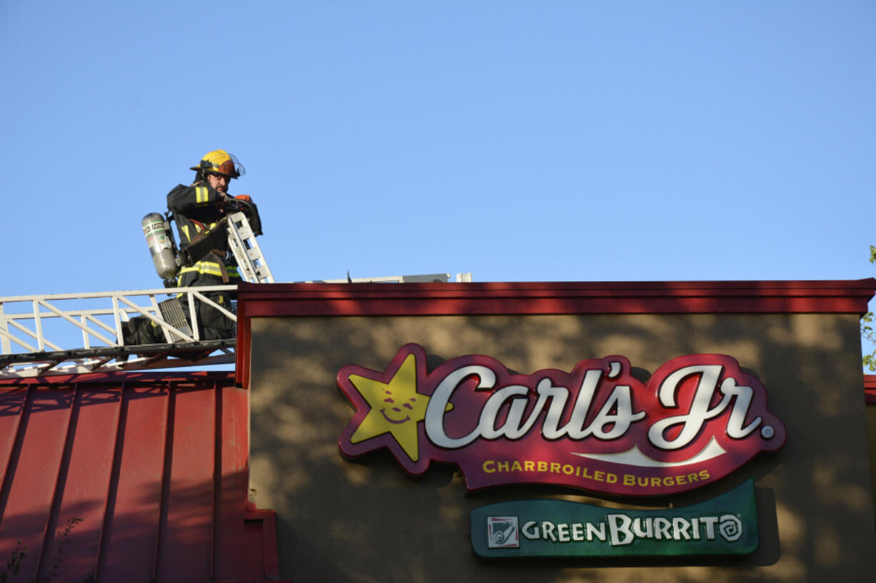 Vancouver firefighter Obie Bowman walks around the roof of a Carl&#039;s Jr. on Fourth Plain Boulevard on Monday evening following a fire there.