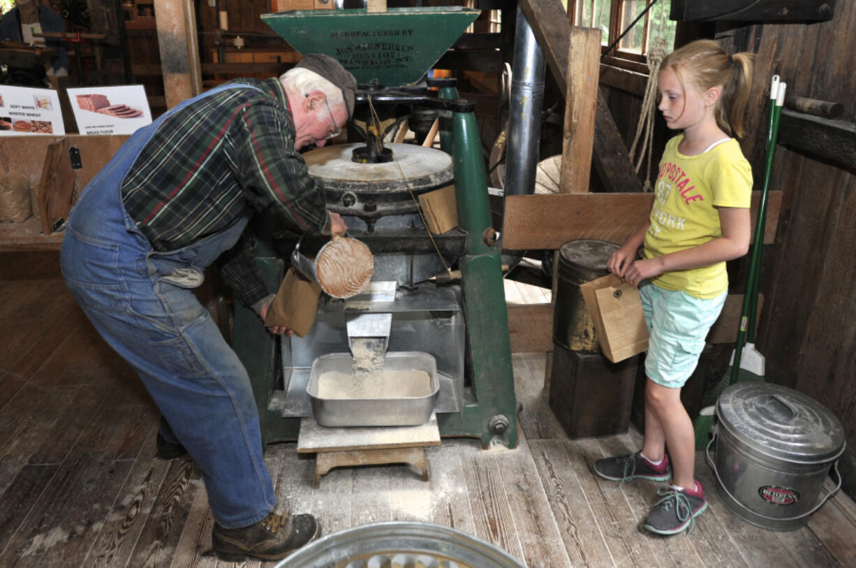 Fred Schulz, left, and volunteer Hadley Meldrum grind grain into flour and fill bags for visitors to take at the Cedar Creek Grist Mill&#039;s Bread and Butter Day on Saturday.