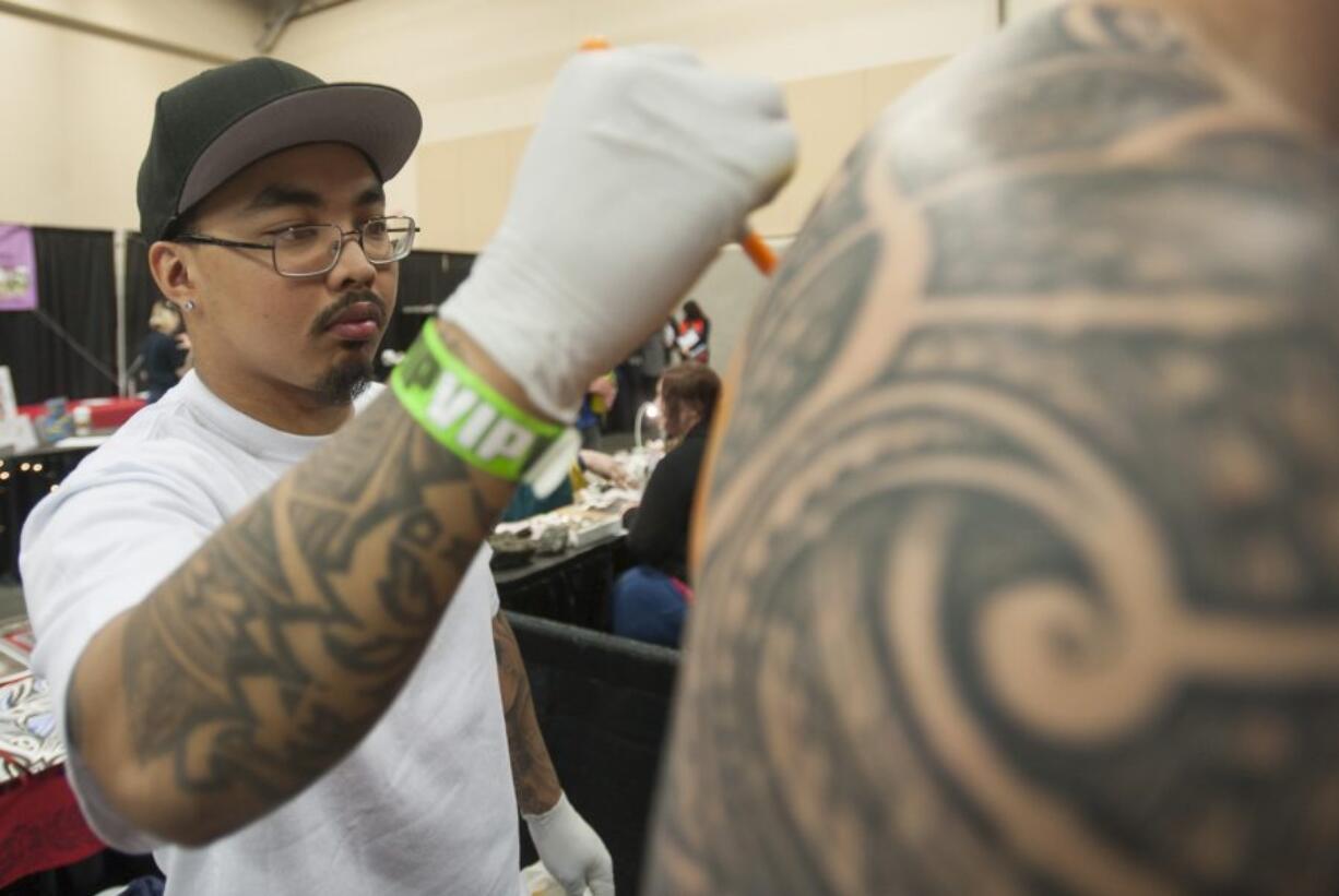 Tattoo artist AJ Tenoril draws an outline on the back of a customer Friday at Ink&#039;n the Couve Tattoo Convention at the Clark County Event Center in Ridgefield.