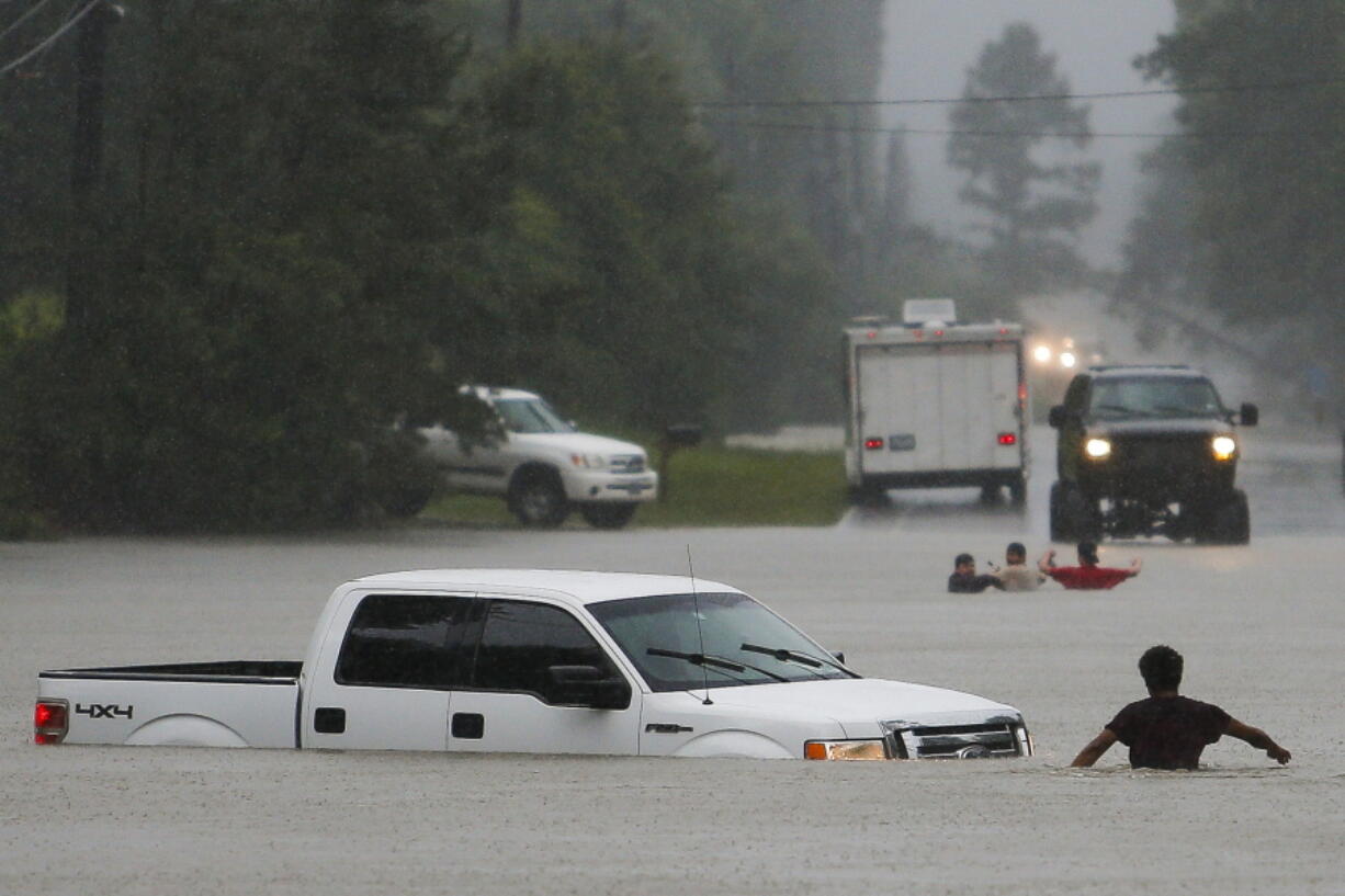 A man wading in floodwater checks to make sure everyone made it out of a truck after the three men in the background drove around a barrier and lost control of the vehicle in rising waters Friday in Magnolia, Texas.