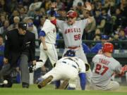 Los Angeles Angels' Mike Trout slides safely into home as Angels' Kole Calhoun (56) reacts to Seattle Mariners catcher Chris Iannetta bobbling the ball on the tag attempt in the eighth inning of a baseball game, Sunday, May 15, 2016, in Seattle. Trout and Calhoun scored on a two-run single hit by Angels' Daniel Nava. (AP Photo/Ted S.