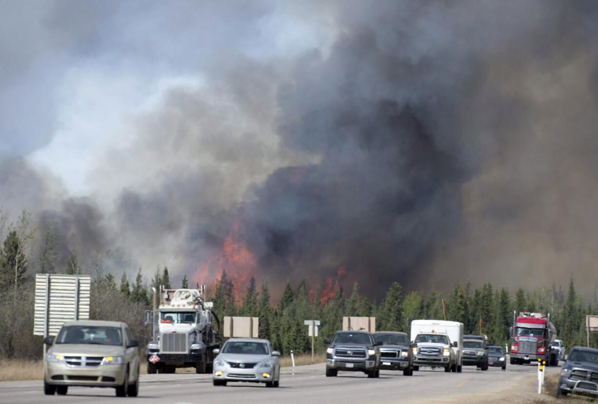 A convoy of cars and trucks pass a wildfire as they are evacuated from Fort McMurray, Alberta, on Highway 63 south of the city on Saturday, May 7, 2016. Canadian officials hoped to complete the mass evacuation of work camps north of Alberta's main oil sands city of Fort McMurray on Saturday, fearing the growing wildfire could double in size and reach a major oil sands mine and even the neighboring province of Saskatchewan.