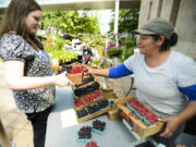 Marcela Munoz, right, from Munoz Berry Farm in Ridgefield, hands a quarter-flat -- six half-pints -- of local berries to Stacey Hall at the Salmon Creek Farmers Market at Legacy Salmon Creek Medical Center on Northeast 139th Street. The market opened for the season Tuesday and will run 11 a.m. to 3 p.m. every Tuesday through September.