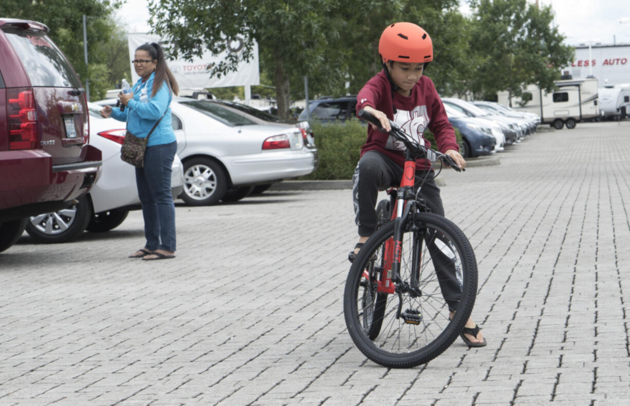 Judah Kadiasang, 9, a student at Crestline Elementary School, tries out his new bike Saturday in the parking lot of McCord&#039;s Vancouver Toyota while his mom, Helen Kadiasang, watches.