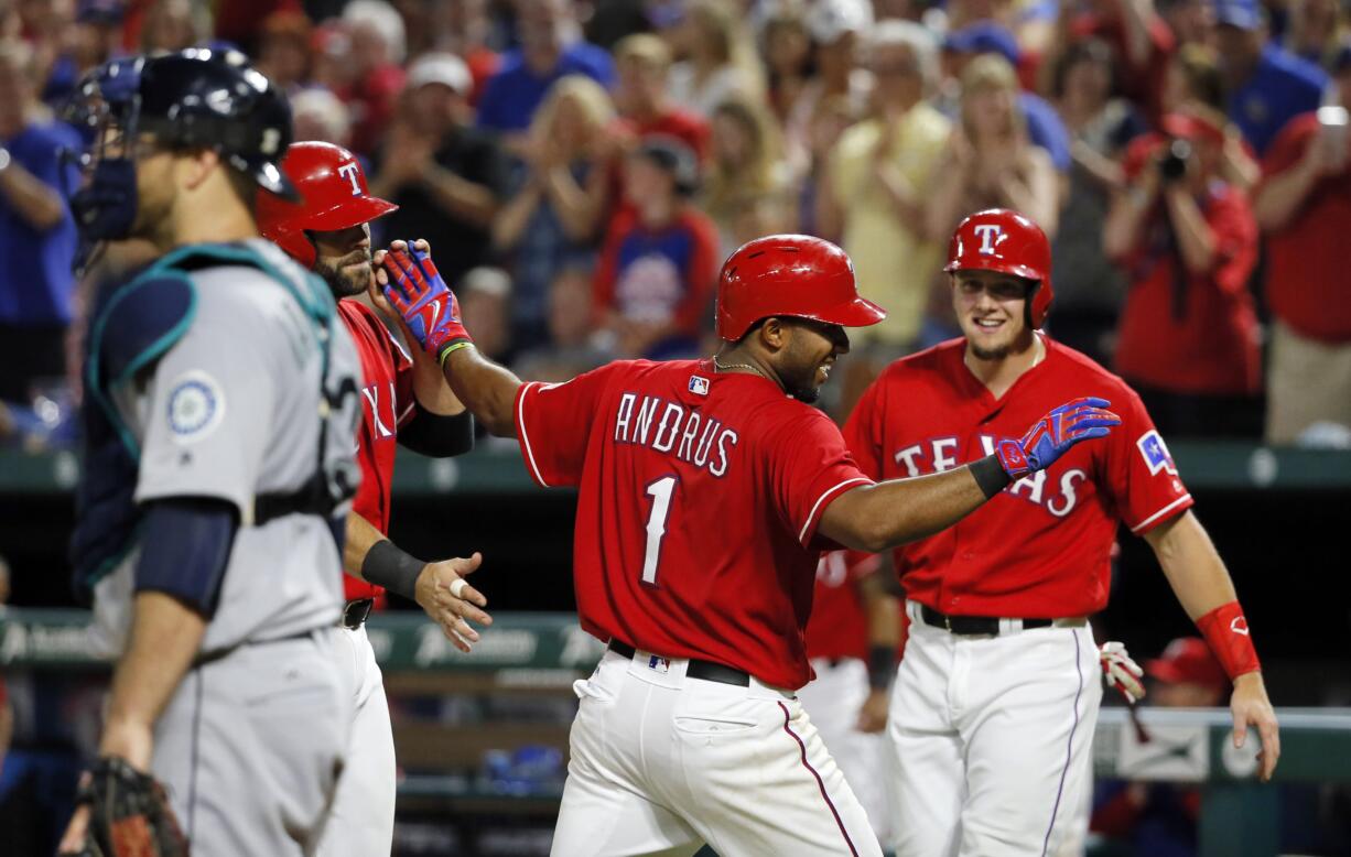 Seattle Mariners catcher Chris Iannetta, left, stands by the plate as Texas Rangers' Mitch Moreland, left rear, Elvis Andrus (1) and Ryan Rua, right rear, celebrate Andrus' three-run home run that scored the duo in the fifth inning of a baseball game, Saturday, June 4, 2016, in Arlington, Texas.