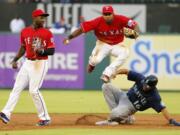 Texas Rangers second baseman Jurickson Profar, left watches as shortstop Elvis Andrus (1) leaps over a sliding Seattle Mariners' Luis Sardinas (16) who was forced by Andrus at second on a fielders choice hit by Norichika Aoki in the third inning of a baseball game on, Friday, June 3, 2016, in Arlington, Texas. Aoki was safe at first on the play.