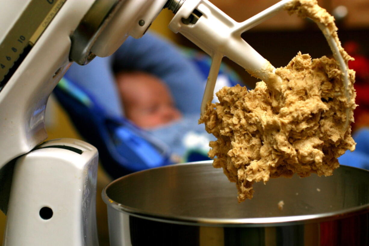 Cookie dough clings to the beaters of a standing mixer.